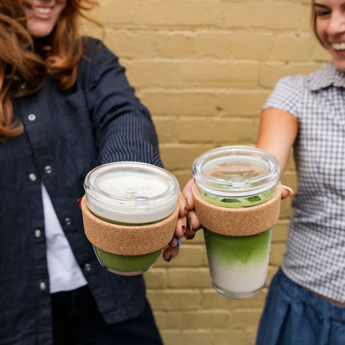 Two women holding KeepCup Brew Cork QuickSip cups filled with layered matcha lattes
