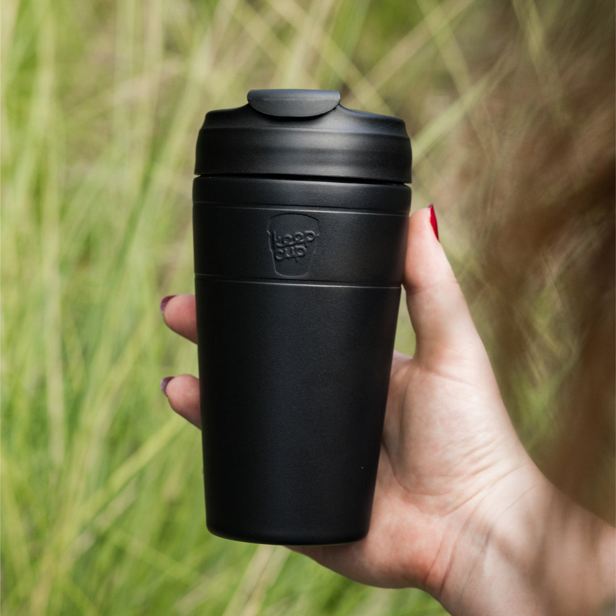 Hand holding a KeepCup Commuter 454ml in Black with matching flip lid