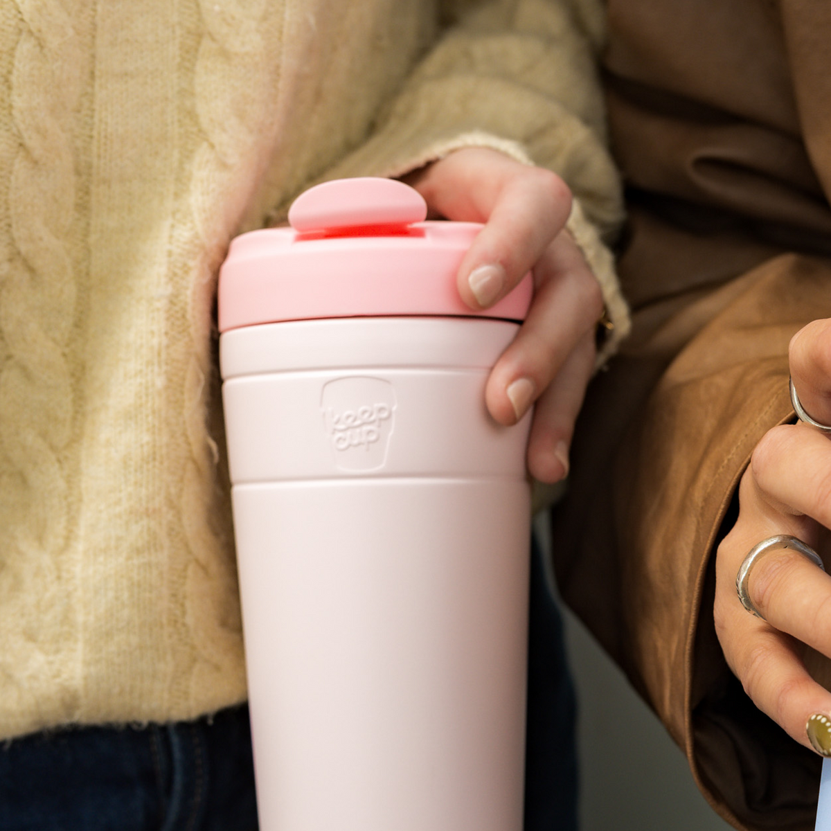 Person in an earth-toned jacket holding a KeepCup Commuter 454ml in Pashmak Pink