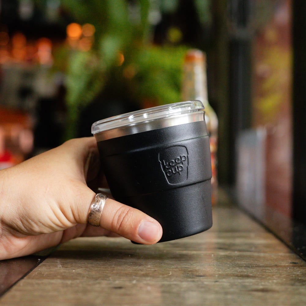 Hand holding a KeepCup Insulated QuickSip Espresso Cup 177ml in Black with clear lid