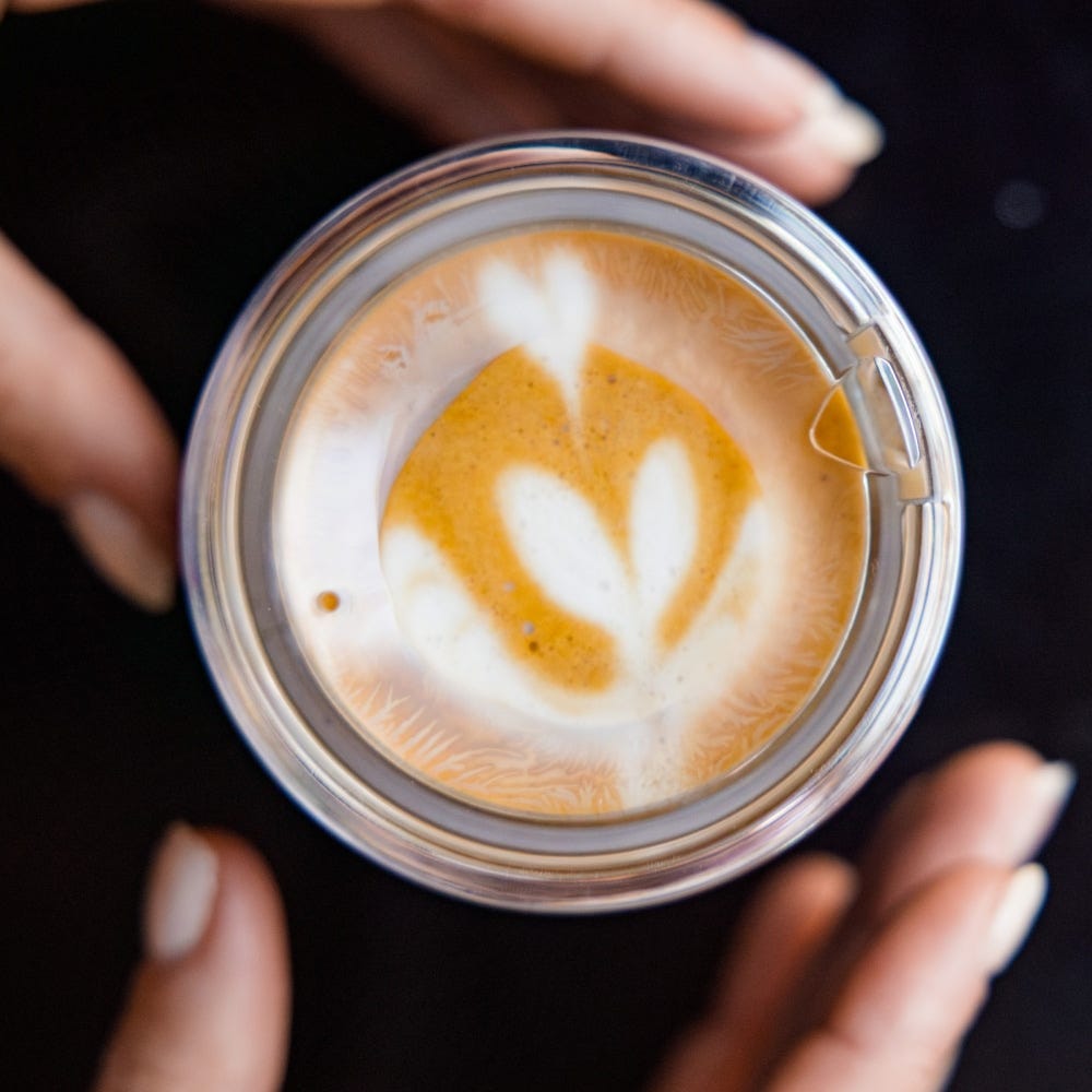 Hands holding a KeepCup Insulated QuickSip Espresso Cup 177ml in Rose with latte art, top view