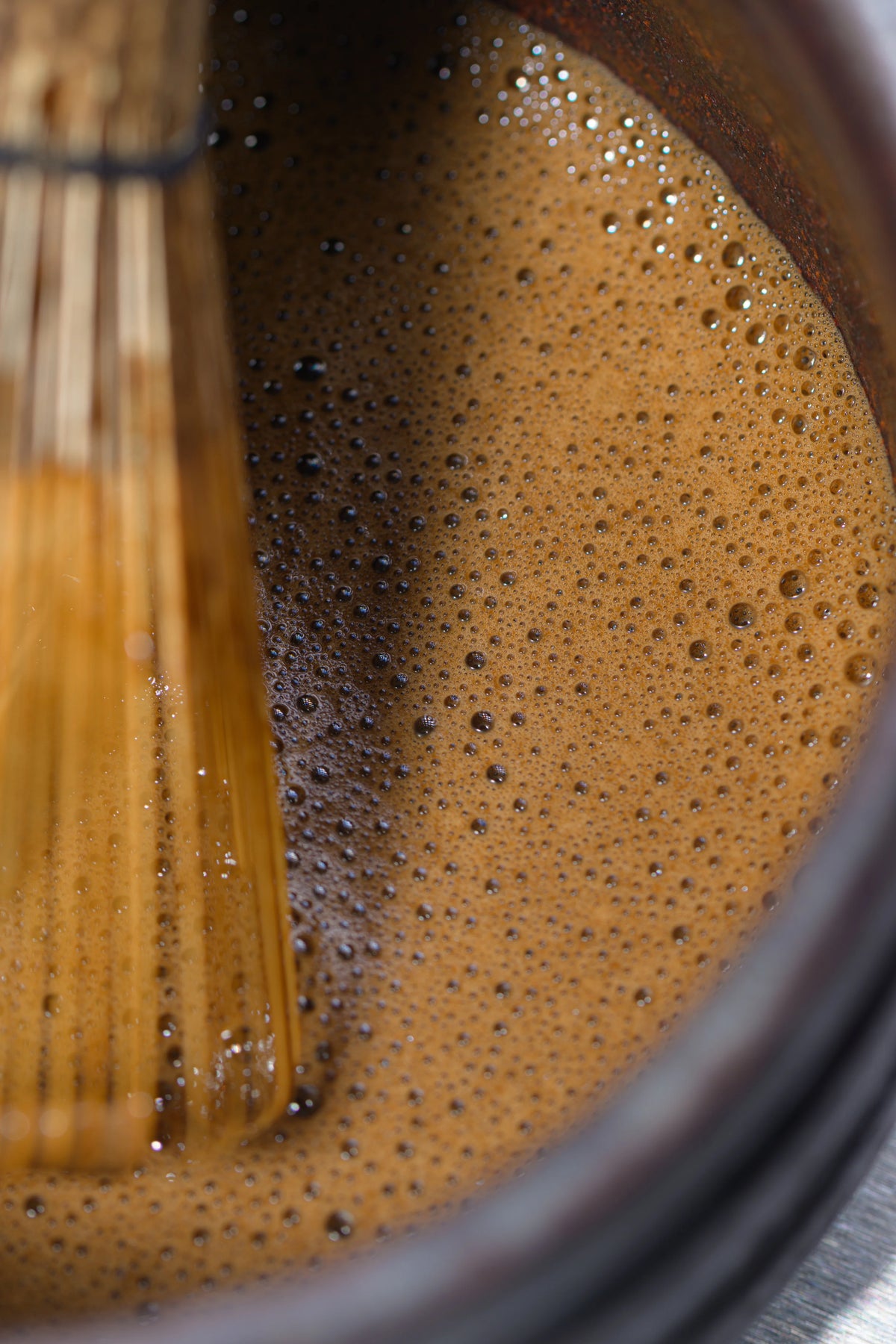 Freshly whisked Uji hojicha with bamboo chasen in a dark bowl