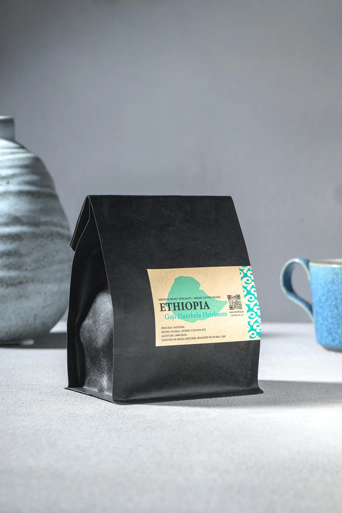 Era Ethiopia Guji Hambela Heirloom coffee bag with teal label beside blue ceramic mug
