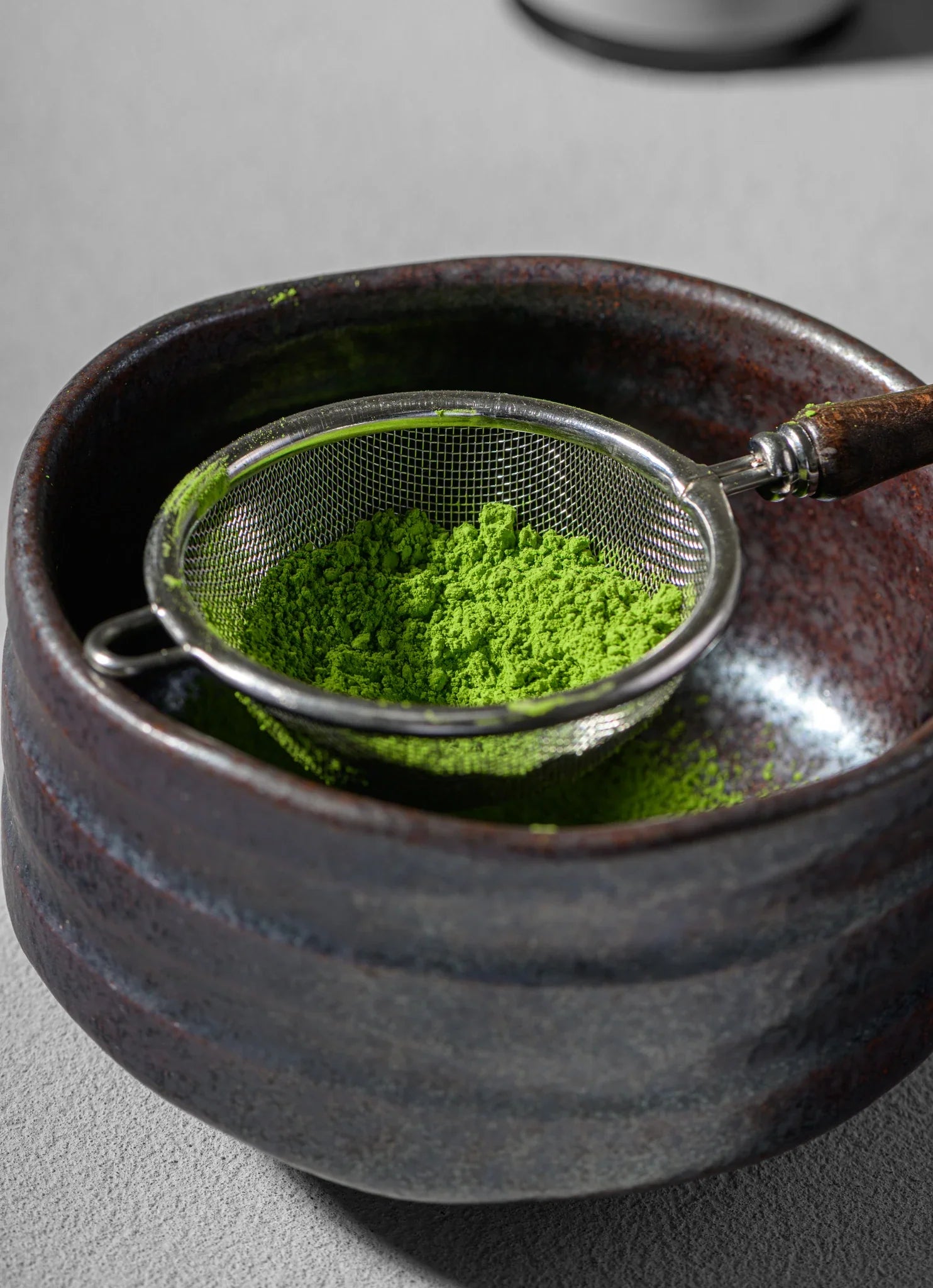 Vibrant green matcha in the Furui sifter resting on a matcha bowl
